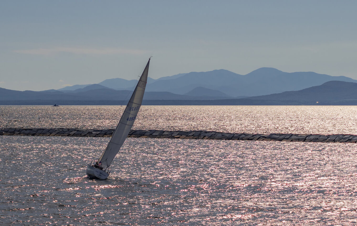 A sailboat on Lake Champlain with the horizon line and mountains clearly visible.