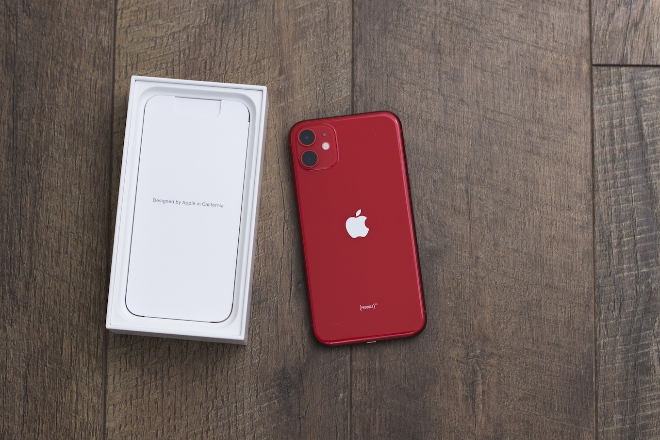 A red iPhone 11 laying next to its box on a wood surface.