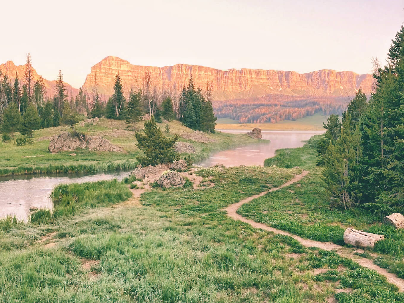 A mountain scene at sunrise showing a field of grass, a river, and a cloudy sky to demonstrate low contrast photography.