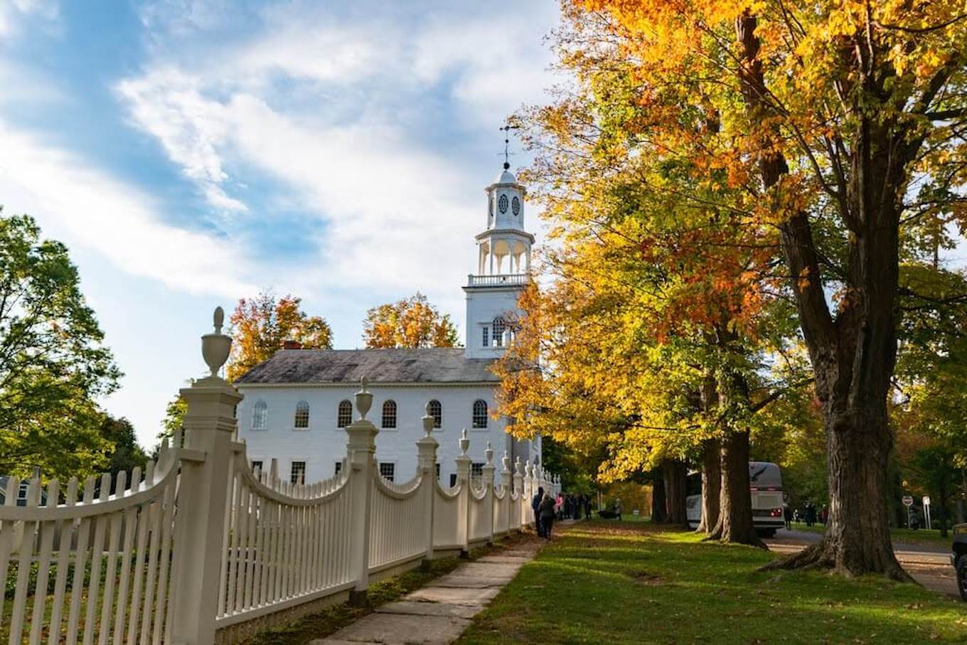 A white church and picket fence framed by fall leaves.