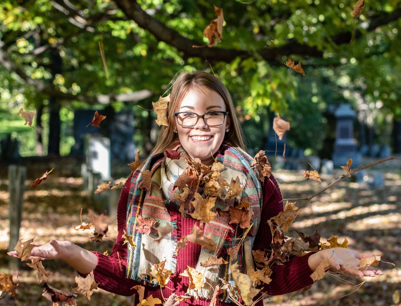 A fall portrait of a woman throwing leaves in the air.