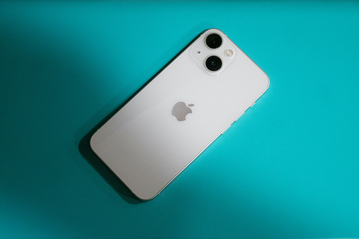 iPhone 13 Mini putih pada permukaan teal